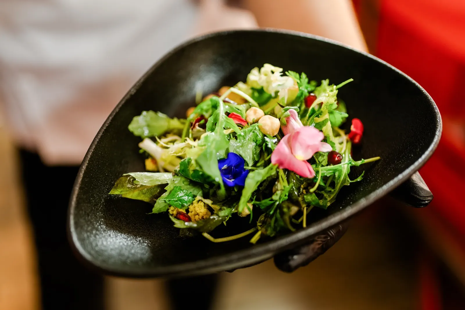 Salat mit essbaren Blüten in einer schwarzen Schale