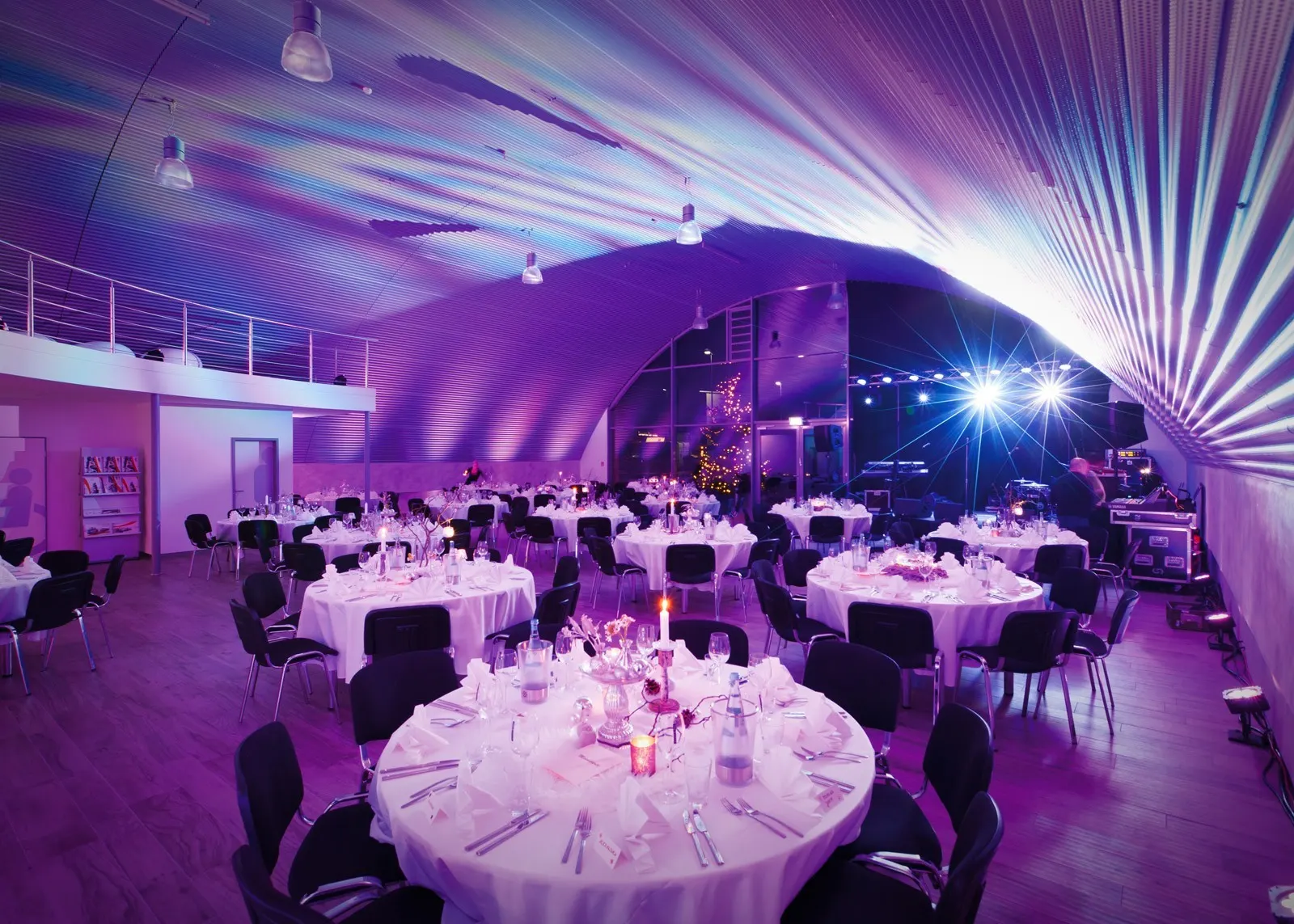 Runde Gala-Tafeln mit weißen Tischdecken im violett beleuchteten Hangar