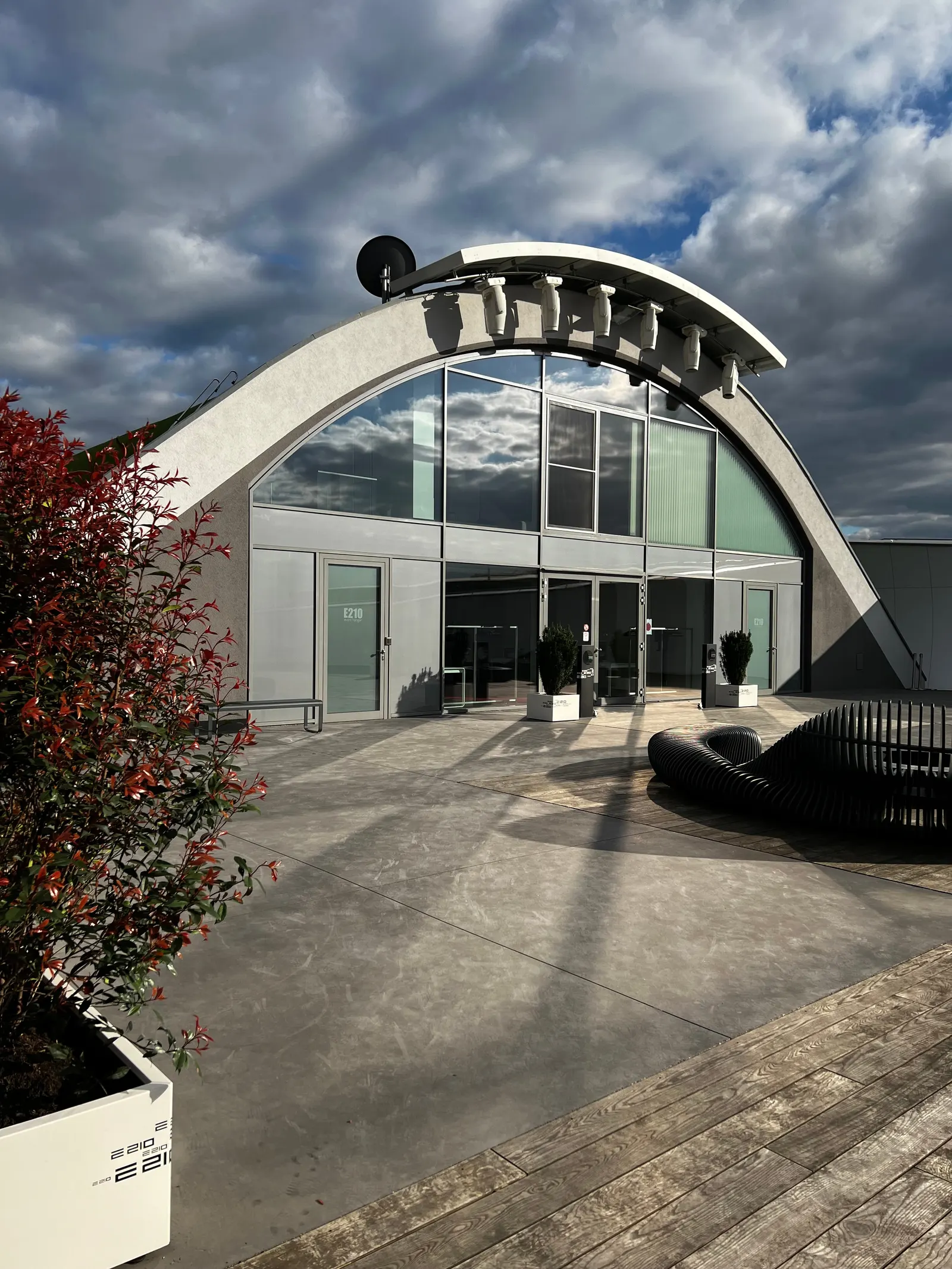 Der E210 Event Hangar von außen: gewölbtes Bogendach mit großer Glasfront unter Wolkenhimmel