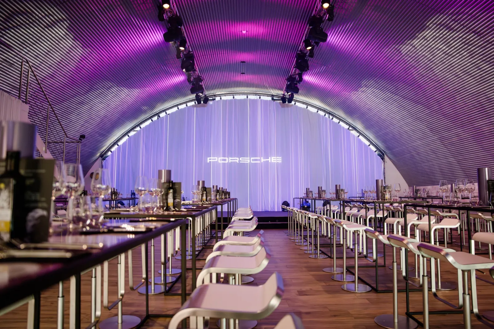 Lange Dinner-Tafeln vor einer Bühne mit Porsche-Schriftzug im violetten Licht