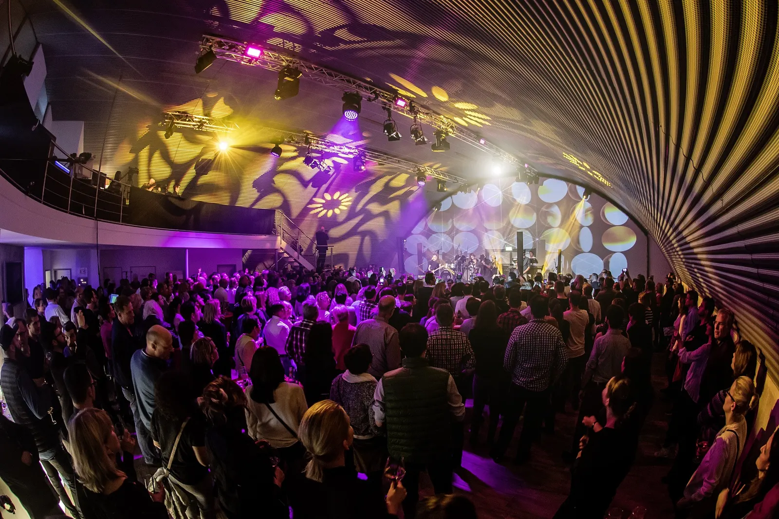 Publikum im Hangar unter einer Lichtshow mit Mustern am Bogendach